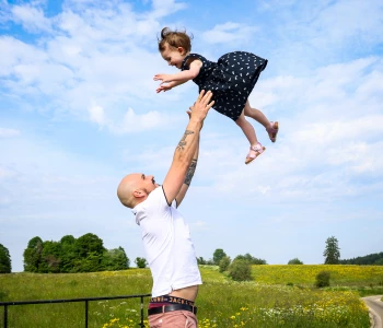 Papa, debout, jette sa petite fille en robe marine à pois blancs à bout de bras dans le ciel bleu